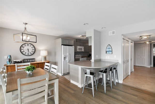 kitchen featuring kitchen peninsula, white appliances, a kitchen breakfast bar, a chandelier, and pendant lighting