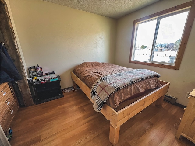 bedroom with dark hardwood / wood-style flooring, a textured ceiling, and a baseboard heating unit