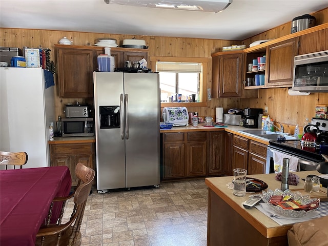 kitchen with wooden walls, sink, stainless steel appliances, and light tile floors