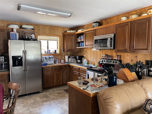 kitchen with wooden walls, sink, stainless steel appliances, and light tile floors