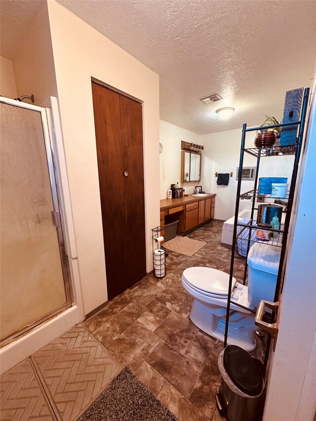 bathroom with tile floors, a shower with shower door, a textured ceiling, vanity, and toilet