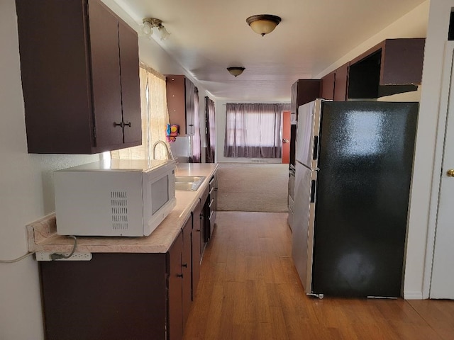 kitchen featuring dark brown cabinets, light hardwood / wood-style floors, stainless steel fridge, and sink