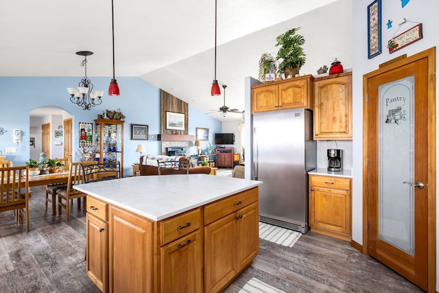 kitchen featuring vaulted ceiling, dark wood-type flooring, decorative light fixtures, a kitchen island, and stainless steel refrigerator