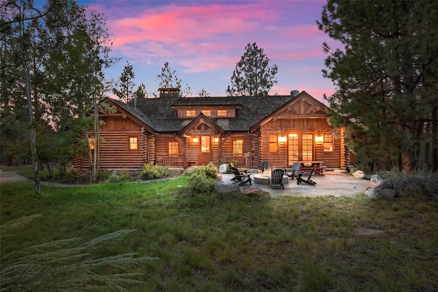 back house at dusk featuring a fire pit, a lawn, and a patio