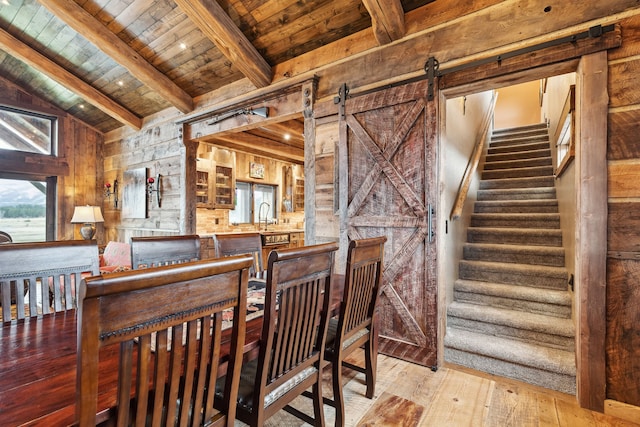 dining space with lofted ceiling with beams, light wood-type flooring, wood ceiling, and a barn door