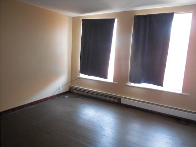 spare room featuring baseboard heating, dark wood-type flooring, and a wealth of natural light