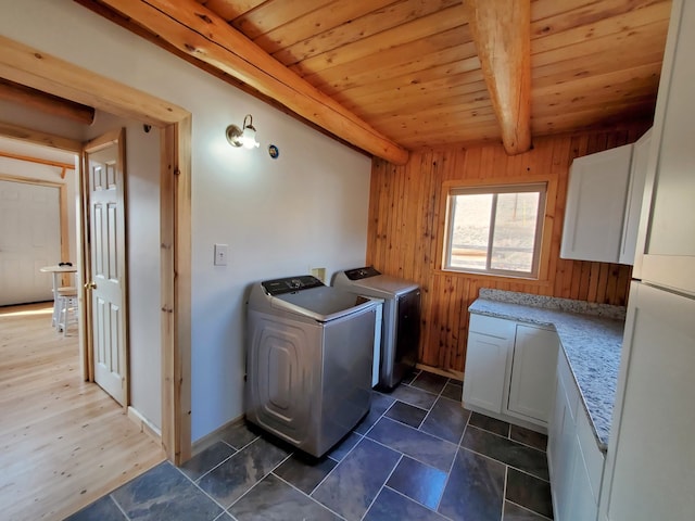 washroom with dark tile flooring, wooden ceiling, wood walls, cabinets, and washing machine and dryer