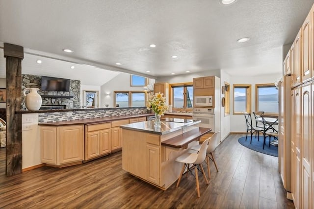 kitchen featuring white appliances, a kitchen island, dark wood-style flooring, light brown cabinetry, and a kitchen bar