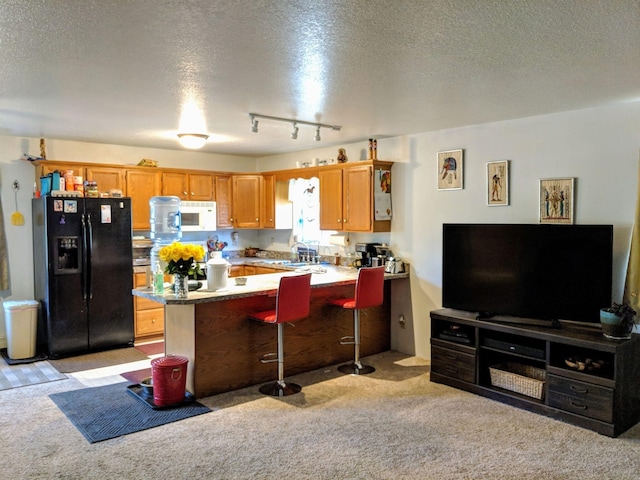 kitchen with light colored carpet, a kitchen breakfast bar, track lighting, a textured ceiling, and black fridge