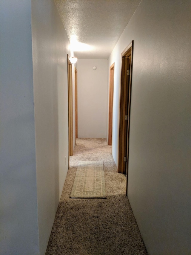 corridor with light colored carpet and a textured ceiling