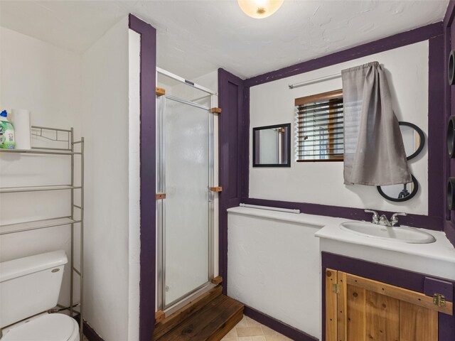 bathroom featuring toilet, vanity with extensive cabinet space, tile flooring, and a shower with shower door