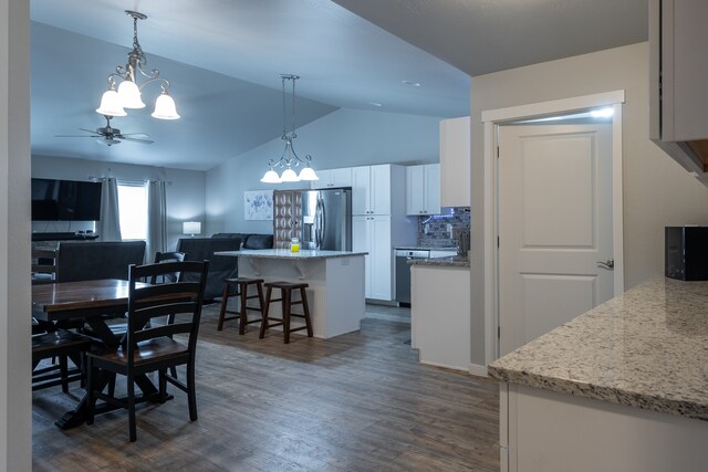 kitchen with white cabinetry, stainless steel fridge, ceiling fan with notable chandelier, dark hardwood / wood-style flooring, and vaulted ceiling