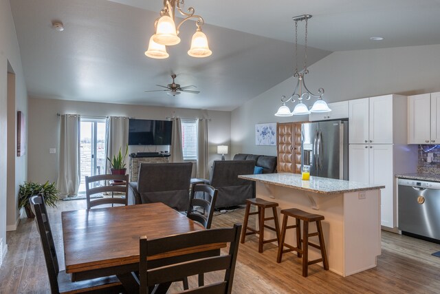 dining area featuring ceiling fan with notable chandelier, light hardwood / wood-style flooring, and lofted ceiling