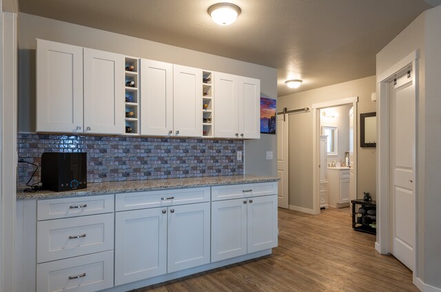 kitchen featuring light stone counters, backsplash, white cabinetry, and wood-type flooring