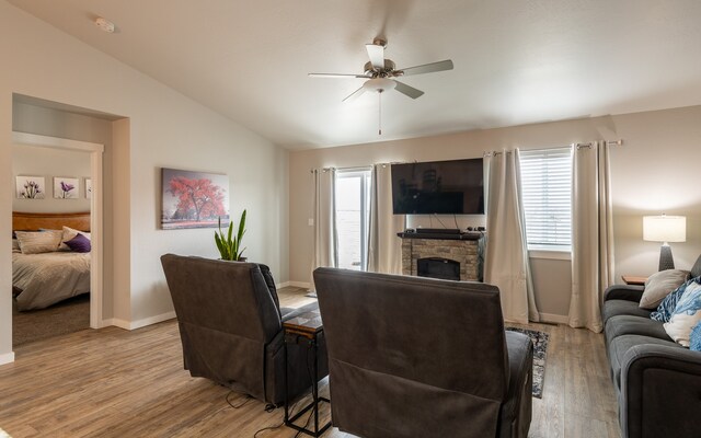 living room featuring ceiling fan, light hardwood / wood-style floors, a fireplace, and vaulted ceiling