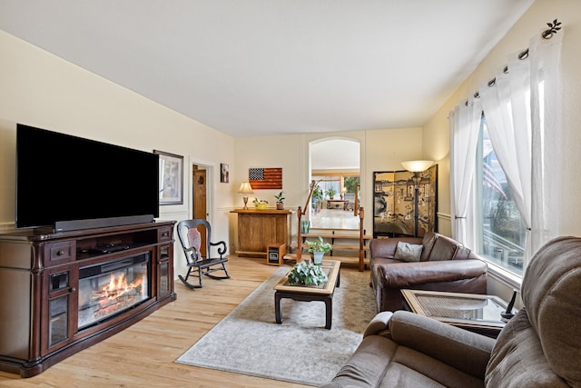 living area with arched walkways, a glass covered fireplace, and light wood-style flooring
