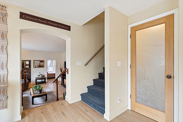 foyer featuring arched walkways, wood finished floors, baseboards, and stairs