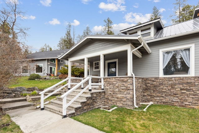 craftsman house featuring covered porch, stone siding, a front lawn, and metal roof