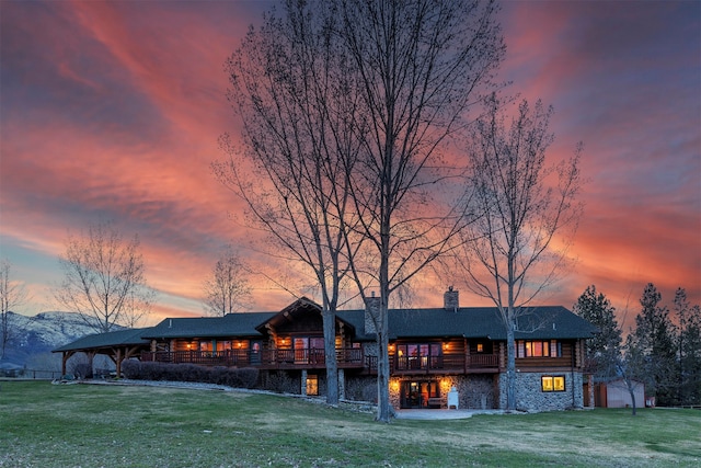 back of property at dusk with an outbuilding, stone siding, a lawn, and a chimney