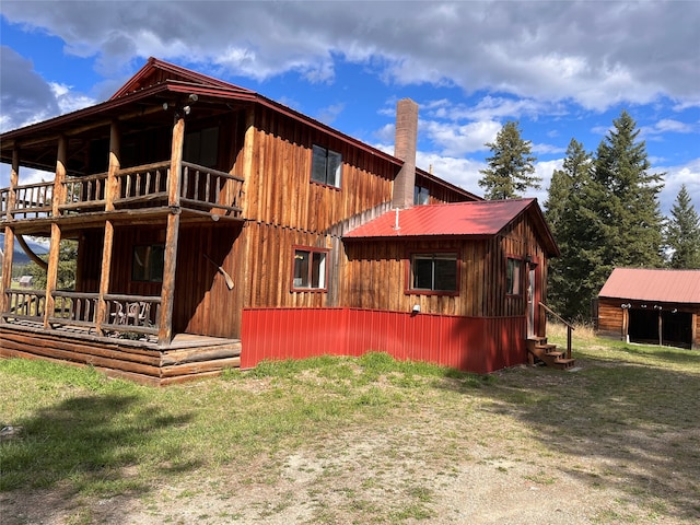 back of property featuring a lawn, a balcony, and an outdoor structure