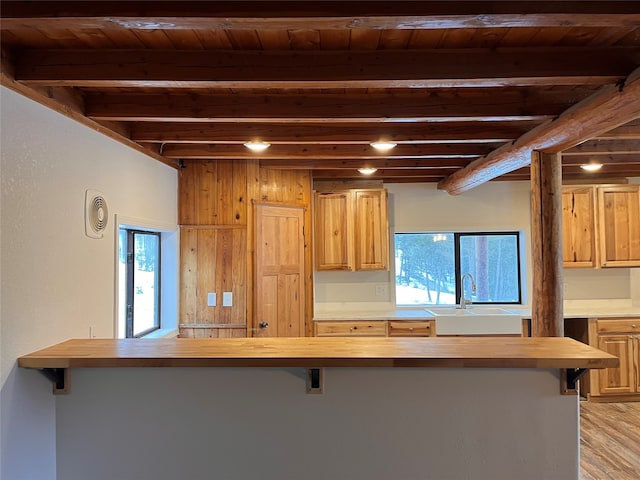 kitchen with a healthy amount of sunlight, light hardwood / wood-style flooring, wooden counters, and beamed ceiling