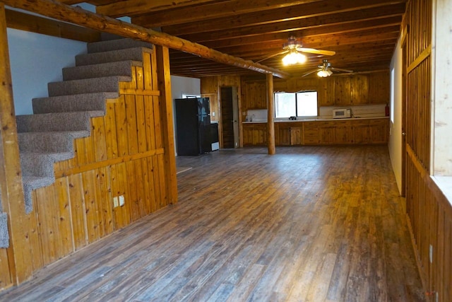 basement with dark hardwood / wood-style flooring, ceiling fan, wood walls, and black fridge