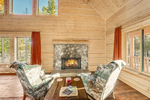 living room with hardwood / wood-style floors, vaulted ceiling, wood walls, a stone fireplace, and wood ceiling