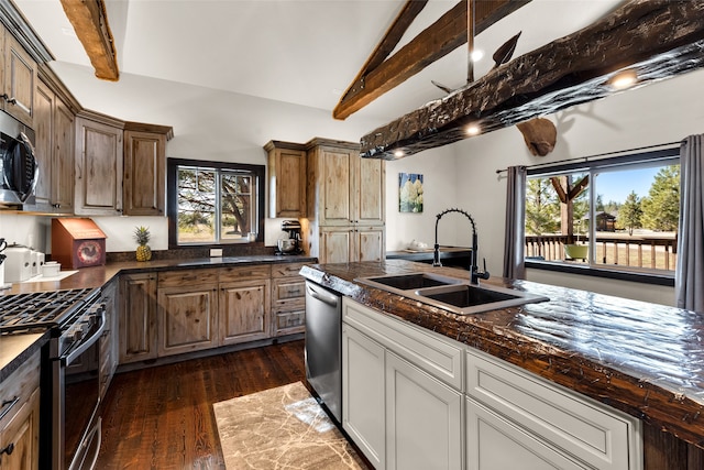 kitchen featuring appliances with stainless steel finishes, sink, vaulted ceiling with beams, dark stone counters, and dark hardwood / wood-style floors