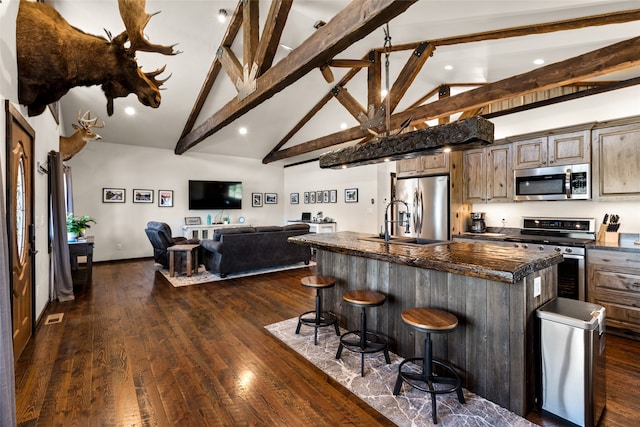 kitchen featuring dark stone countertops, dark wood-type flooring, appliances with stainless steel finishes, a kitchen breakfast bar, and a kitchen island with sink