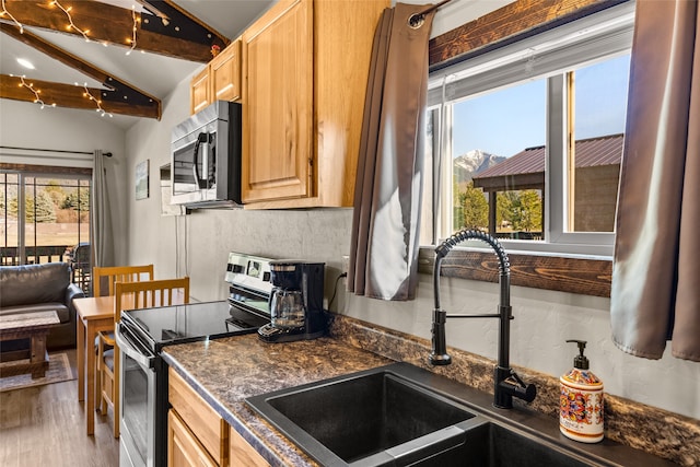 kitchen with lofted ceiling with beams, appliances with stainless steel finishes, light wood-type flooring, and sink