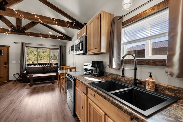 kitchen featuring appliances with stainless steel finishes, dark hardwood / wood-style floors, dark stone countertops, lofted ceiling with beams, and sink