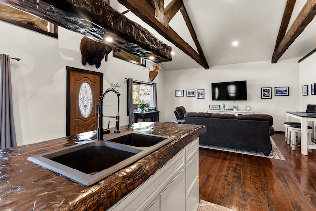 kitchen with sink, vaulted ceiling with beams, dark stone counters, white cabinetry, and dark hardwood / wood-style floors