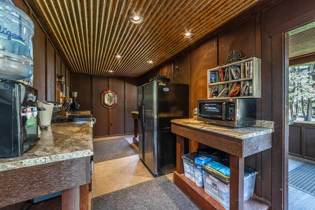 kitchen with wooden ceiling, dark brown cabinetry, black refrigerator, and wooden walls