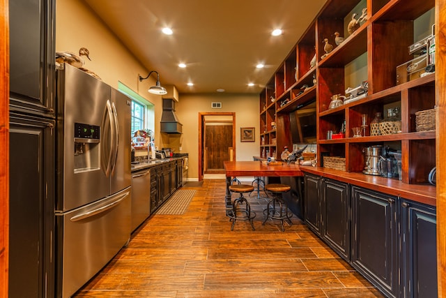 kitchen with a kitchen bar, custom exhaust hood, light wood-type flooring, and stainless steel appliances