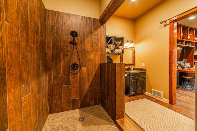 bathroom with walk in shower, wood walls, vanity, and hardwood / wood-style flooring