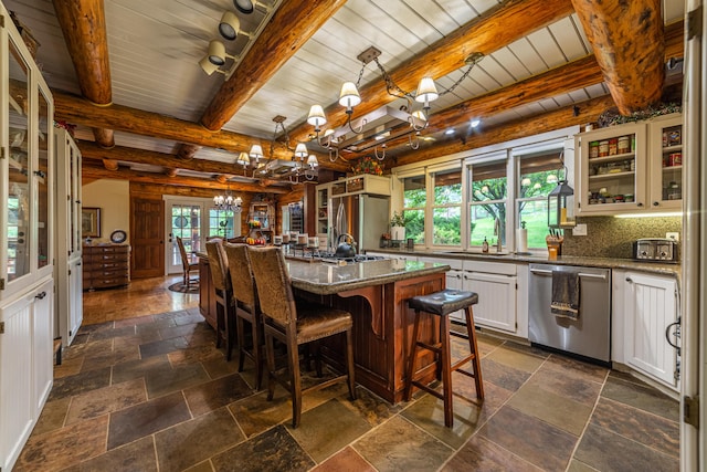 interior space featuring pendant lighting, white cabinetry, stainless steel appliances, beam ceiling, and an island with sink