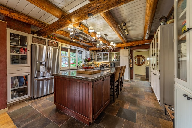 kitchen with stainless steel refrigerator with ice dispenser, a center island, beam ceiling, and dark stone counters