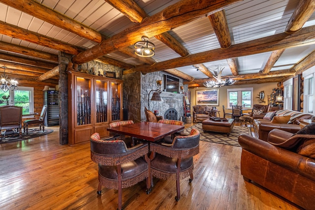 dining space with beamed ceiling, dark hardwood / wood-style floors, a notable chandelier, and a stone fireplace