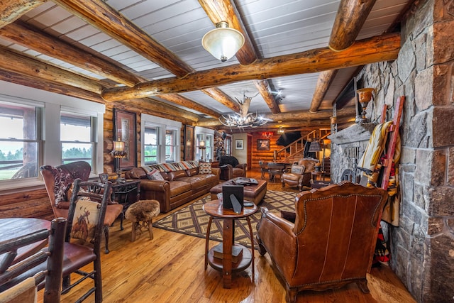 living room with beamed ceiling, a fireplace, light wood-type flooring, a chandelier, and rustic walls