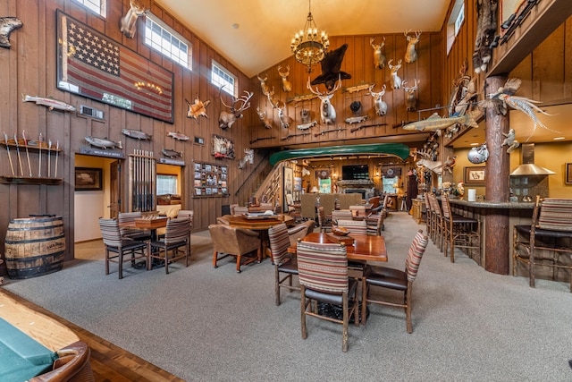 living room featuring high vaulted ceiling, an inviting chandelier, carpet floors, and wooden walls