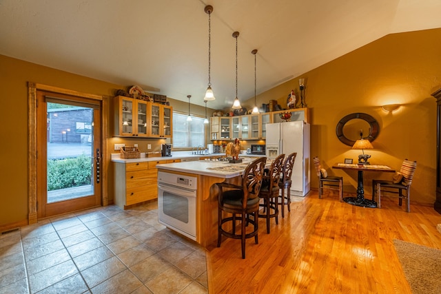 kitchen with decorative light fixtures, white appliances, vaulted ceiling, a center island, and a breakfast bar