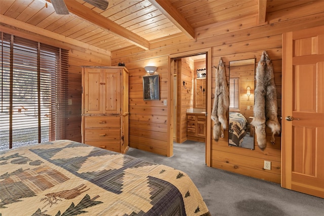 carpeted bedroom with ensuite bath, beam ceiling, ceiling fan, and wooden walls