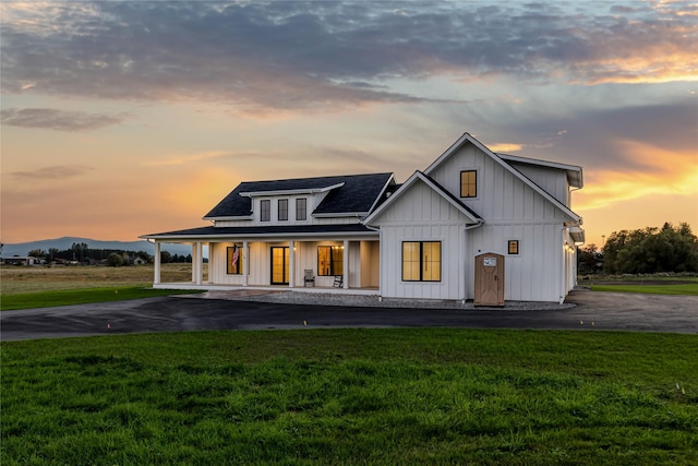 1052 Foxtail Dr, Kalispell, MT 59901 - back of house at dusk featuring driveway, board and batten siding, a shingled roof, a porch, and a yard