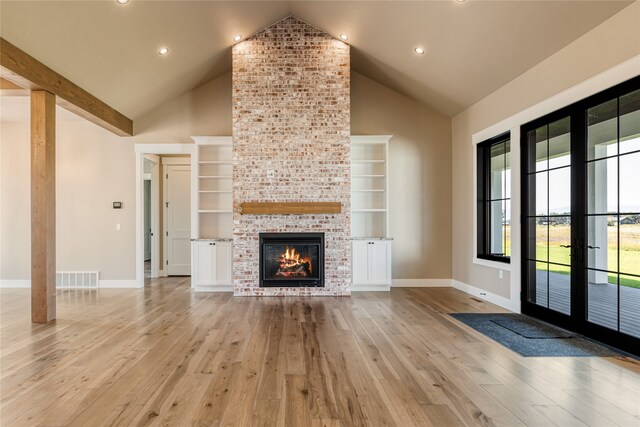 unfurnished living room with light hardwood / wood-style flooring, high vaulted ceiling, a brick fireplace, and french doors