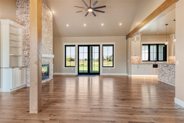 1052 Foxtail Dr, Kalispell, MT 59901 - unfurnished living room with high vaulted ceiling, a ceiling fan, light wood-style floors, a large fireplace, and baseboards