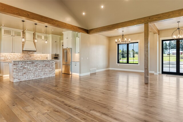 unfurnished living room with a notable chandelier, light wood-type flooring, and lofted ceiling with beams