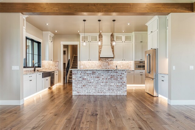 kitchen featuring light hardwood / wood-style flooring, stainless steel appliances, light stone counters, premium range hood, and a kitchen island