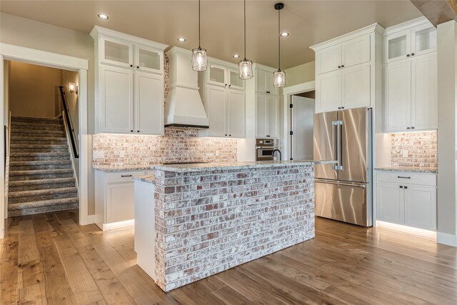 kitchen with light wood-type flooring, appliances with stainless steel finishes, premium range hood, and an island with sink