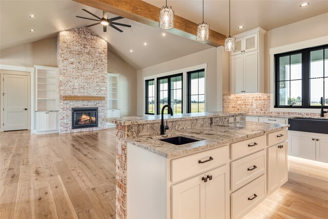 kitchen featuring light hardwood / wood-style flooring, sink, a stone fireplace, and beam ceiling