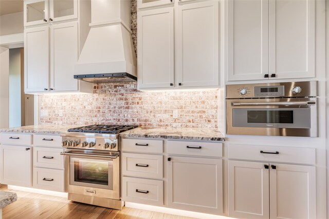 kitchen featuring light wood-type flooring, white cabinets, appliances with stainless steel finishes, and premium range hood